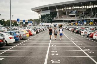 Parking officiel du Stade Pierre Mauroy avec des voitures garées et des supporters marchant vers l'entrée du stade